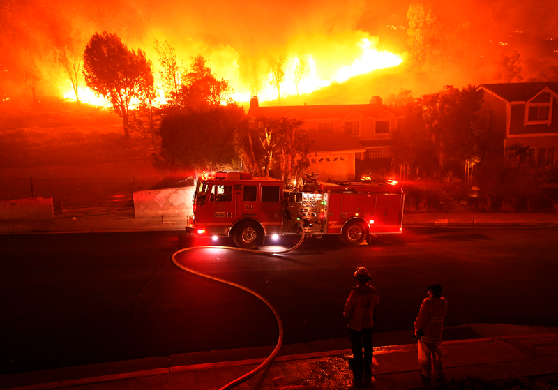 Los Angeles County firefighter looks on as the out-of-control Woolsey Fire explodes behind a house in the West Hills neighborhood on November 9, 2018 in Los Angeles, California.